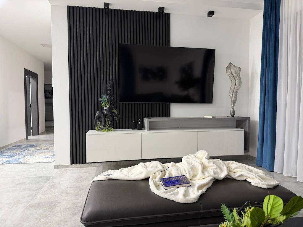 Modernes Wohnzimmer mit großem Fernseher an einer eleganten Lamellenwand und schwebendem Medienschrank.