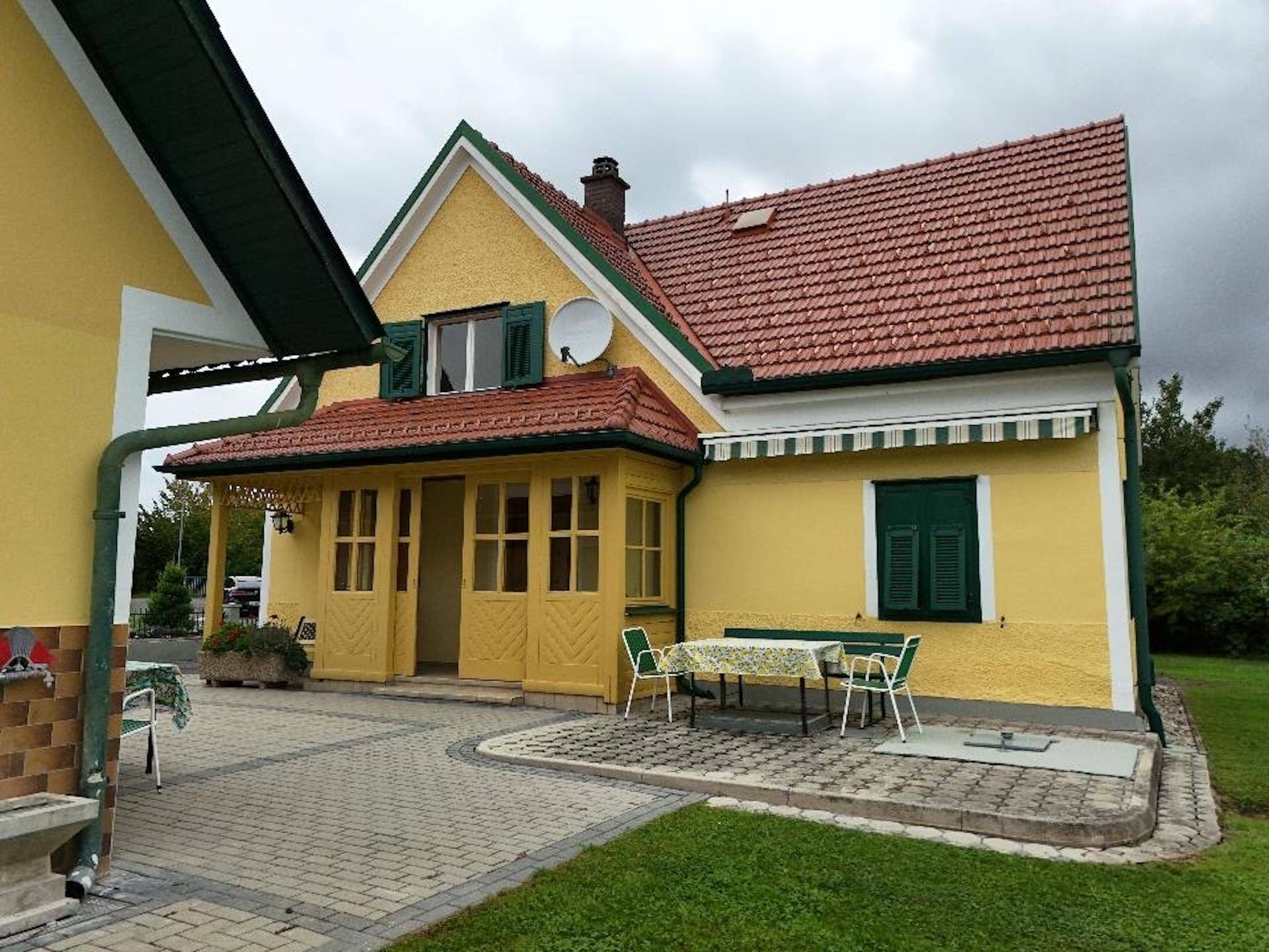 Gemütliche Terrasse mit Gartenmöbeln und Markise, angrenzend an das gelbe Wohnhaus.