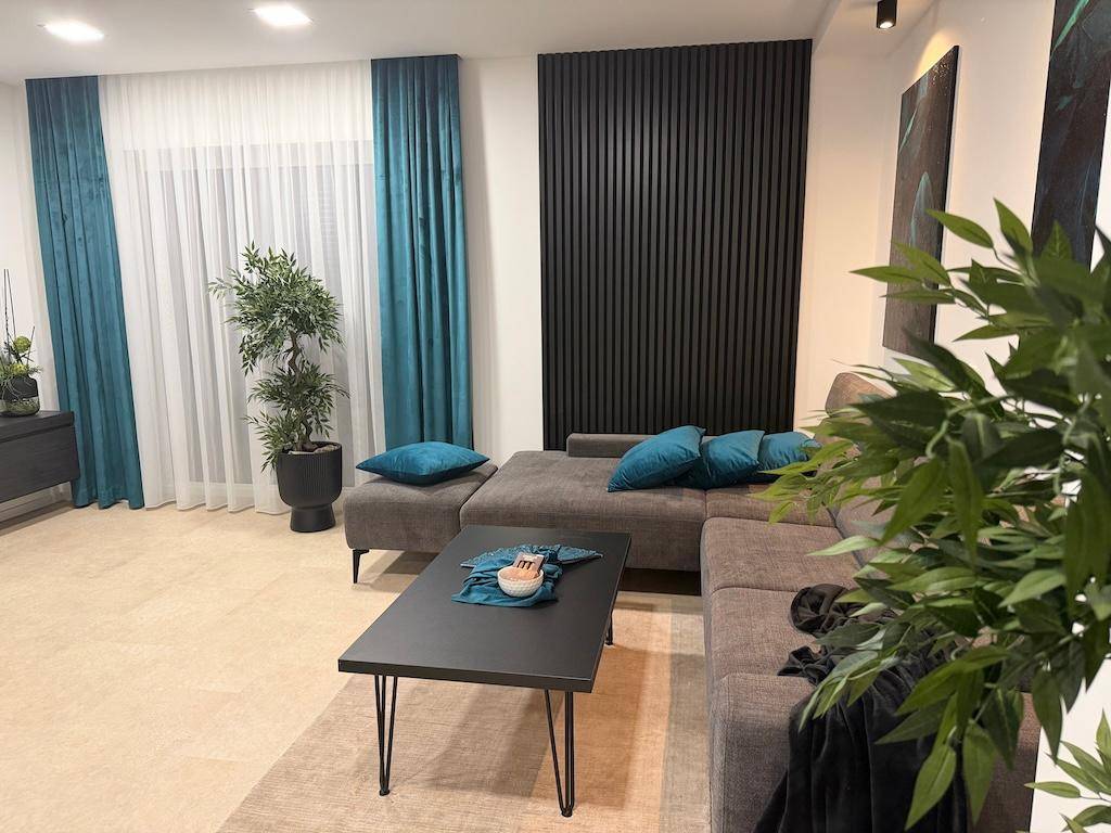 Helles Wohnzimmer mit beigem Sofa, grünen Pflanzen und dekorativen blauen Kissen.