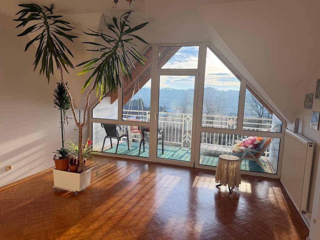 Helles Wohnzimmer im Dachgeschoss mit großen Fenstern und Panoramablick auf die Landschaft.