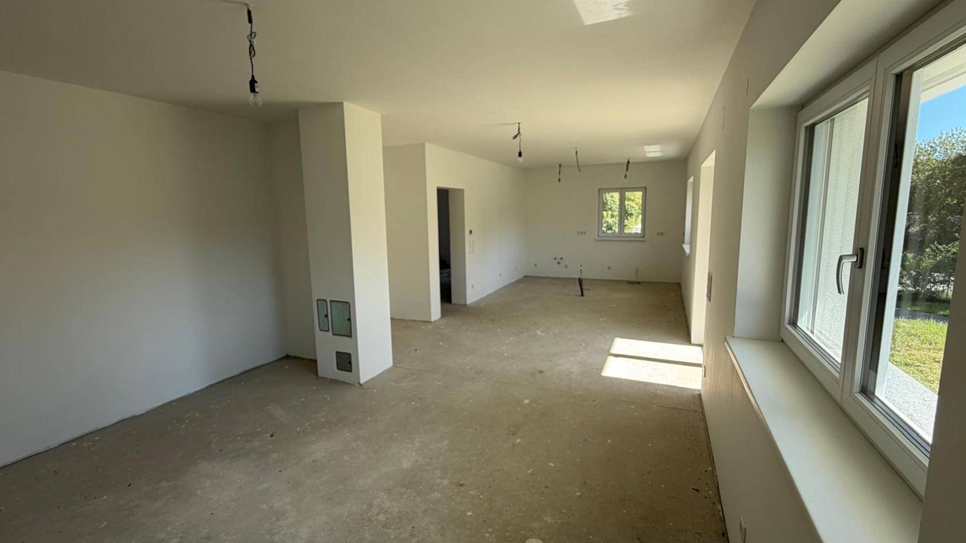 Großer, heller Wohnbereich im Rohbau mit vielen Fenstern und einer tragenden Säule.