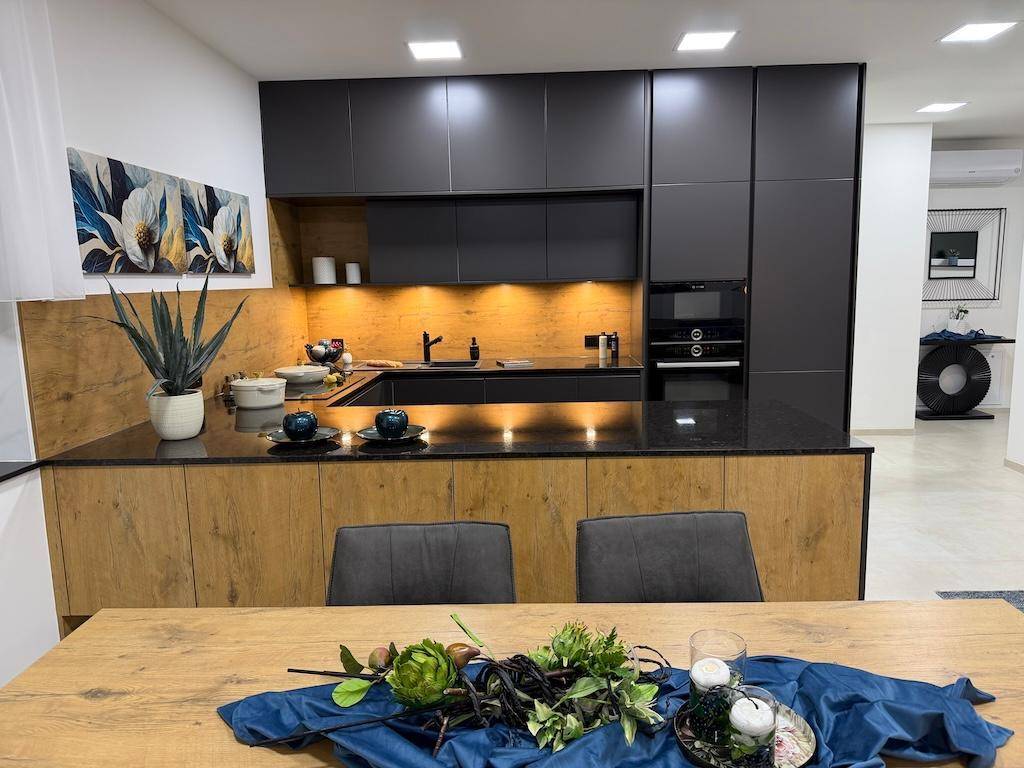 Moderne Küche mit dunklen Schränken, Holzrückwand und großem Esstisch im Vordergrund.