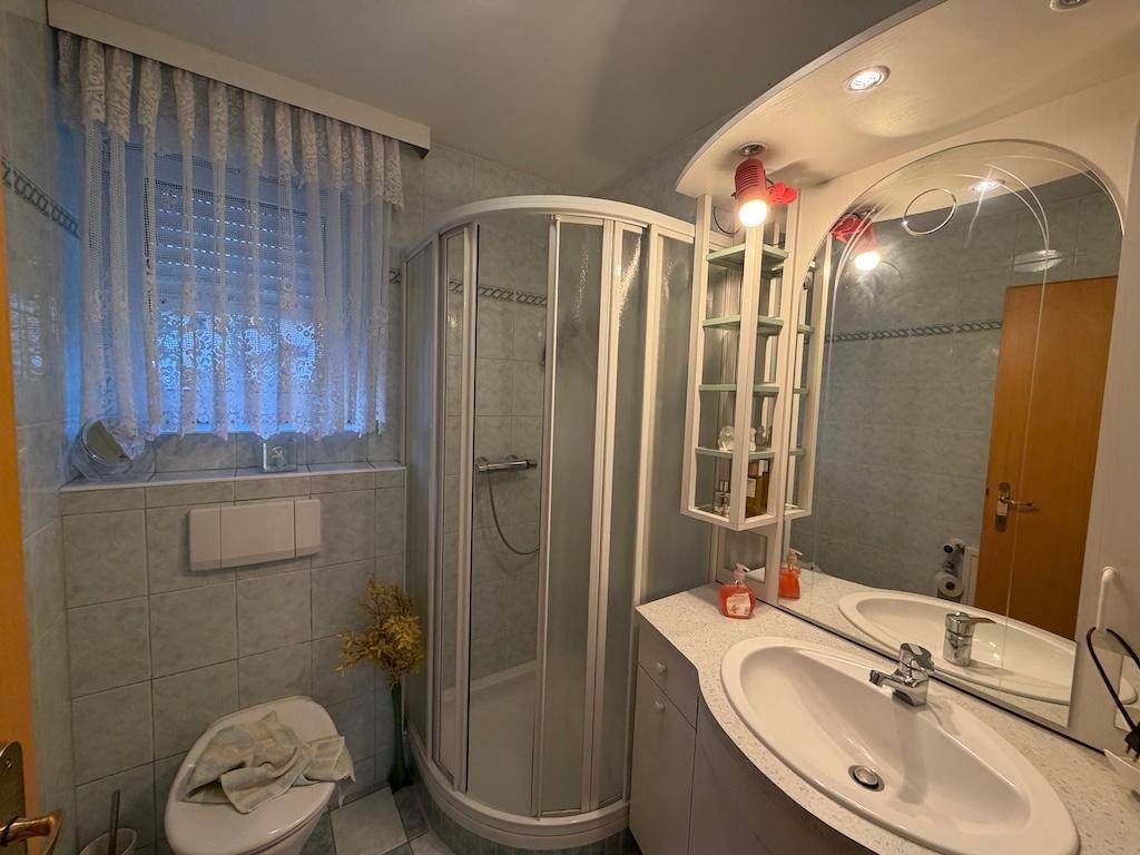 Badezimmer mit Eckdusche, Waschtisch, WC und Spiegelschrank in hellblauen Fliesen.
