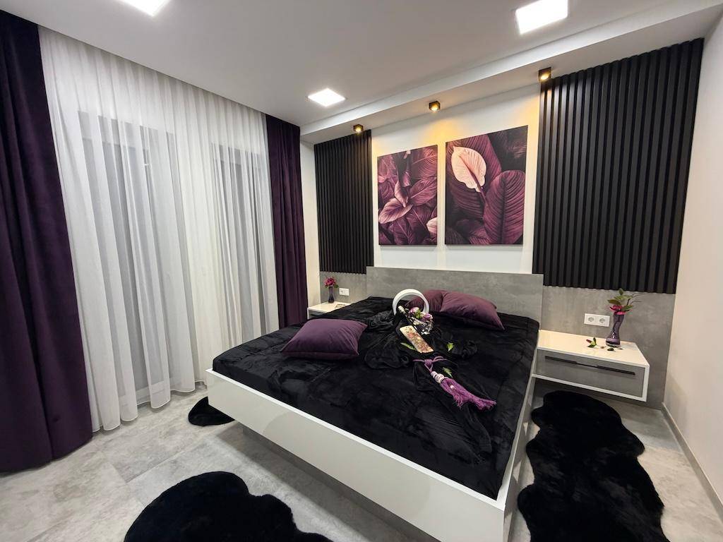 Geräumiges Schlafzimmer mit modernem Bett, stilvollen Wandleuchten und großen Fenstern mit Vorhängen.