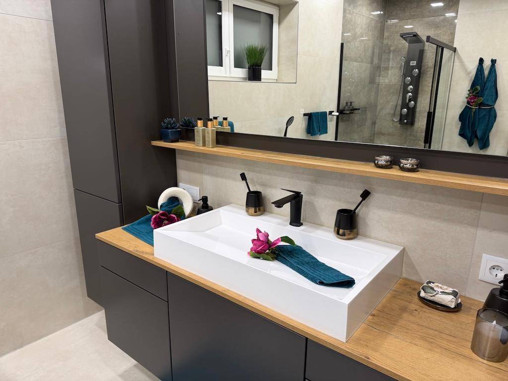 Modernes Badezimmer mit Aufsatzwaschbecken, großem Spiegel und Holzablage.
