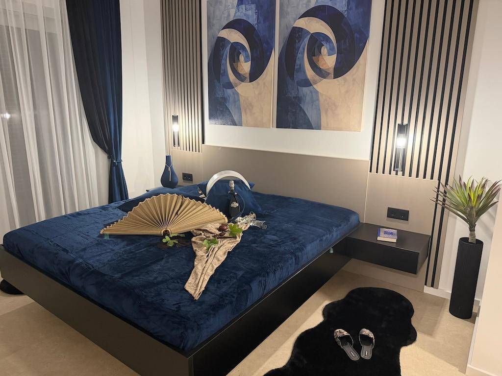 Modernes Schlafzimmer mit großem Bett, blauer Bettwäsche und dekorativen Wandpaneelen.