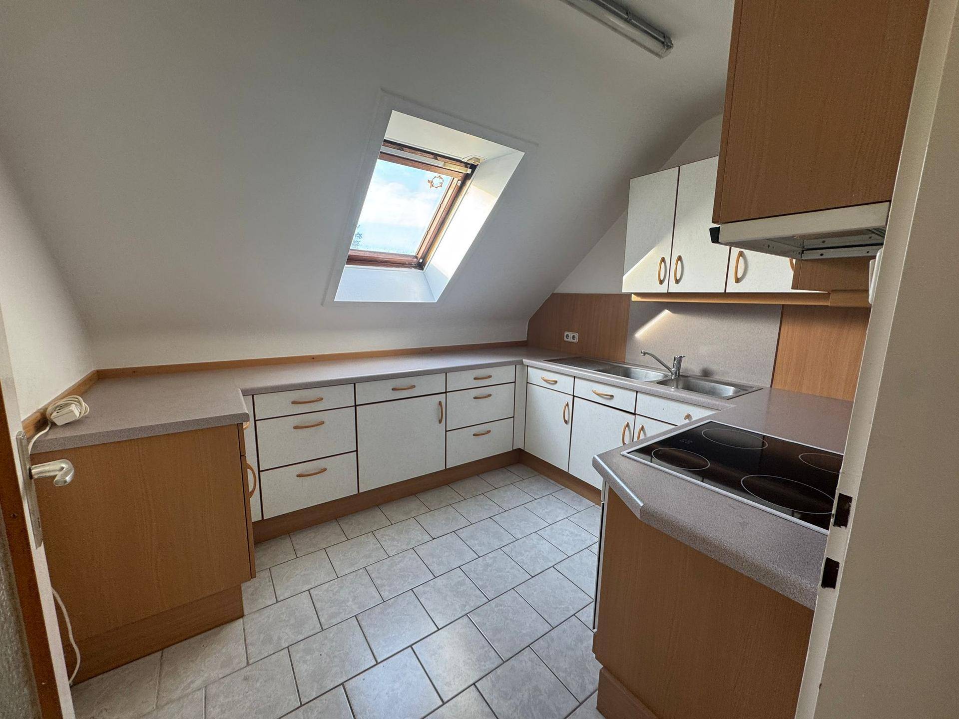 Dachgeschossküche mit Einbauschränken, Fliesenboden und einem Dachfenster für natürliches Licht.