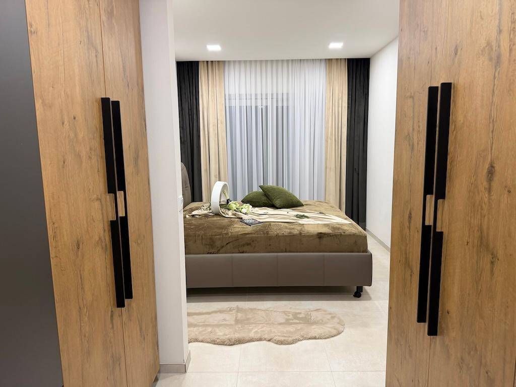 Blick vom begehbaren Kleiderschrank auf das moderne Schlafzimmer mit großem Bett und Fenster.