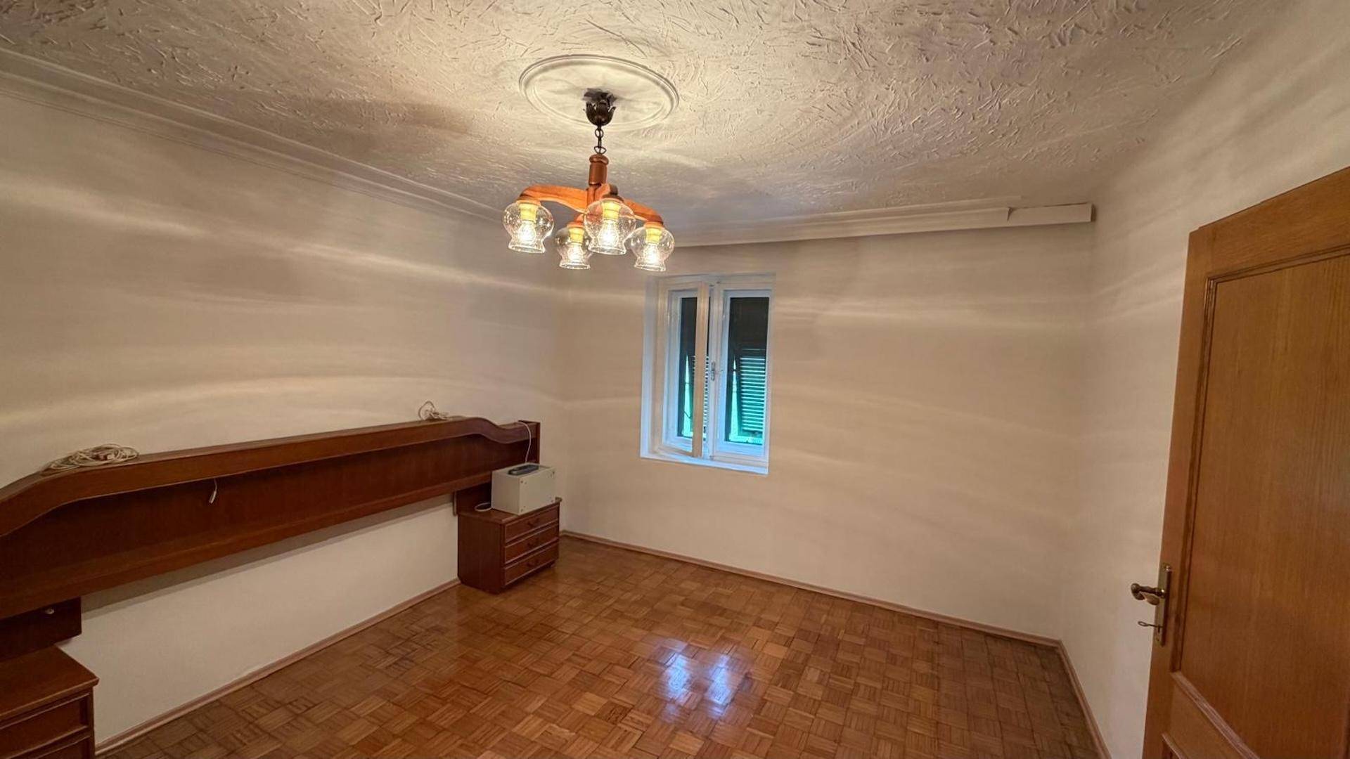 Schlafzimmer mit Parkettboden, strukturiertem Deckenputz und einem Fenster, das Tageslicht hereinlässt.