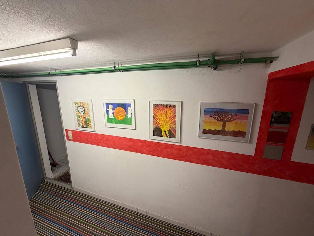 Kellerflur mit bunten Kinderzeichnungen an der Wand und gestreiftem Teppichboden.