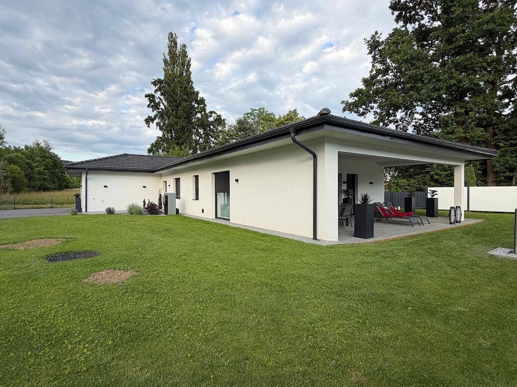Modernes Einfamilienhaus mit weitläufigem Rasen und großer überdachter Terrasse, umgeben von viel Grün.