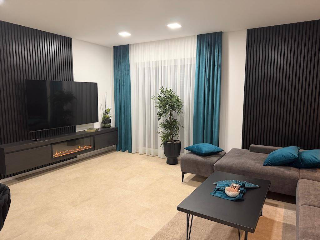 Offener Wohnbereich mit großem Fernseher, Elektrokamin und beigem Ecksofa.