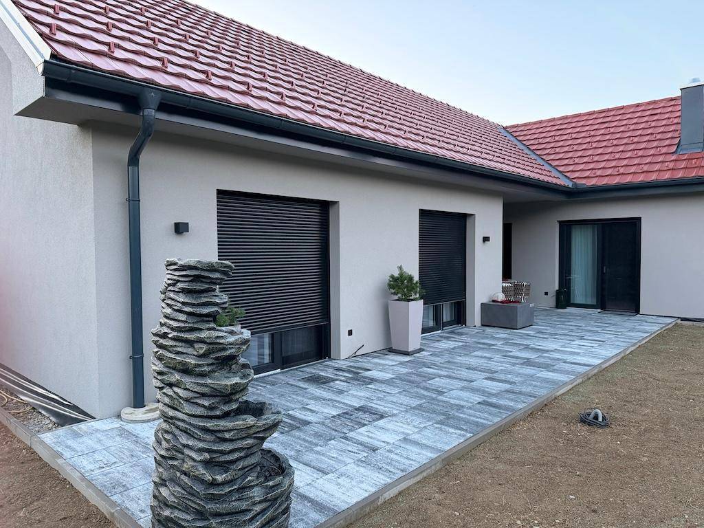 Moderne Terrasse mit dekorativem Steinfbrunnen und Rollläden an den Fenstern des Hauses.
