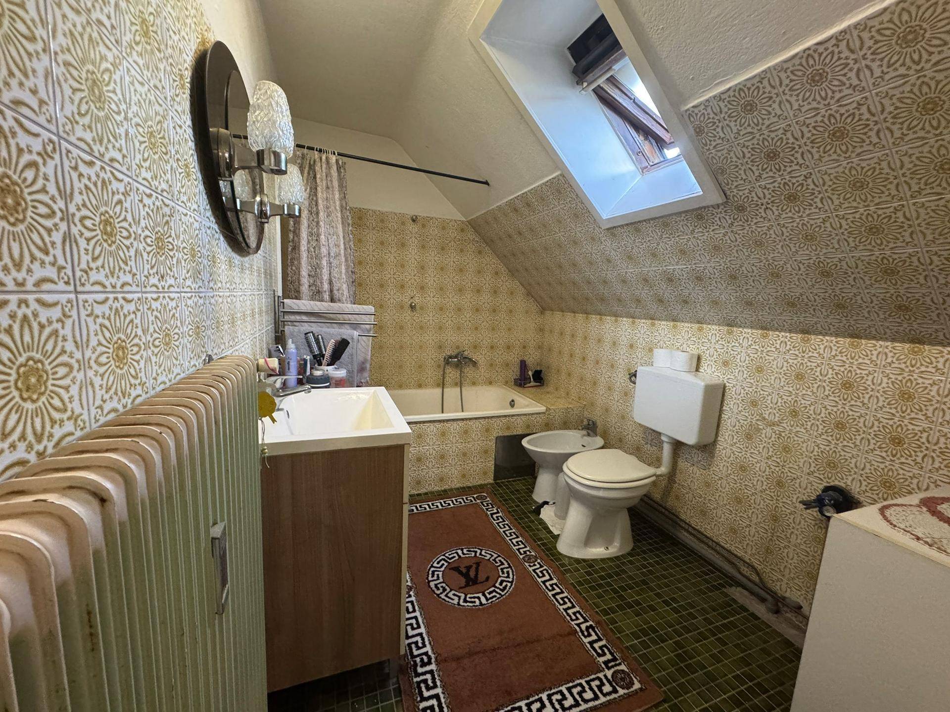 Badezimmer im Dachgeschoss mit Badewanne, Bidet, WC und gemusterten Fliesen.