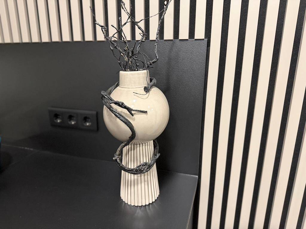 Dekorative Vase mit Zweigen auf der dunklen Küchenarbeitsplatte vor einer Holzlamellenwand.