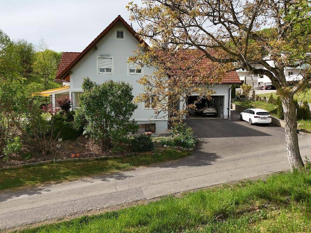 Wohnhaus mit Garage, Auffahrt und umgebender Natur, eingebettet in eine grüne Landschaft.