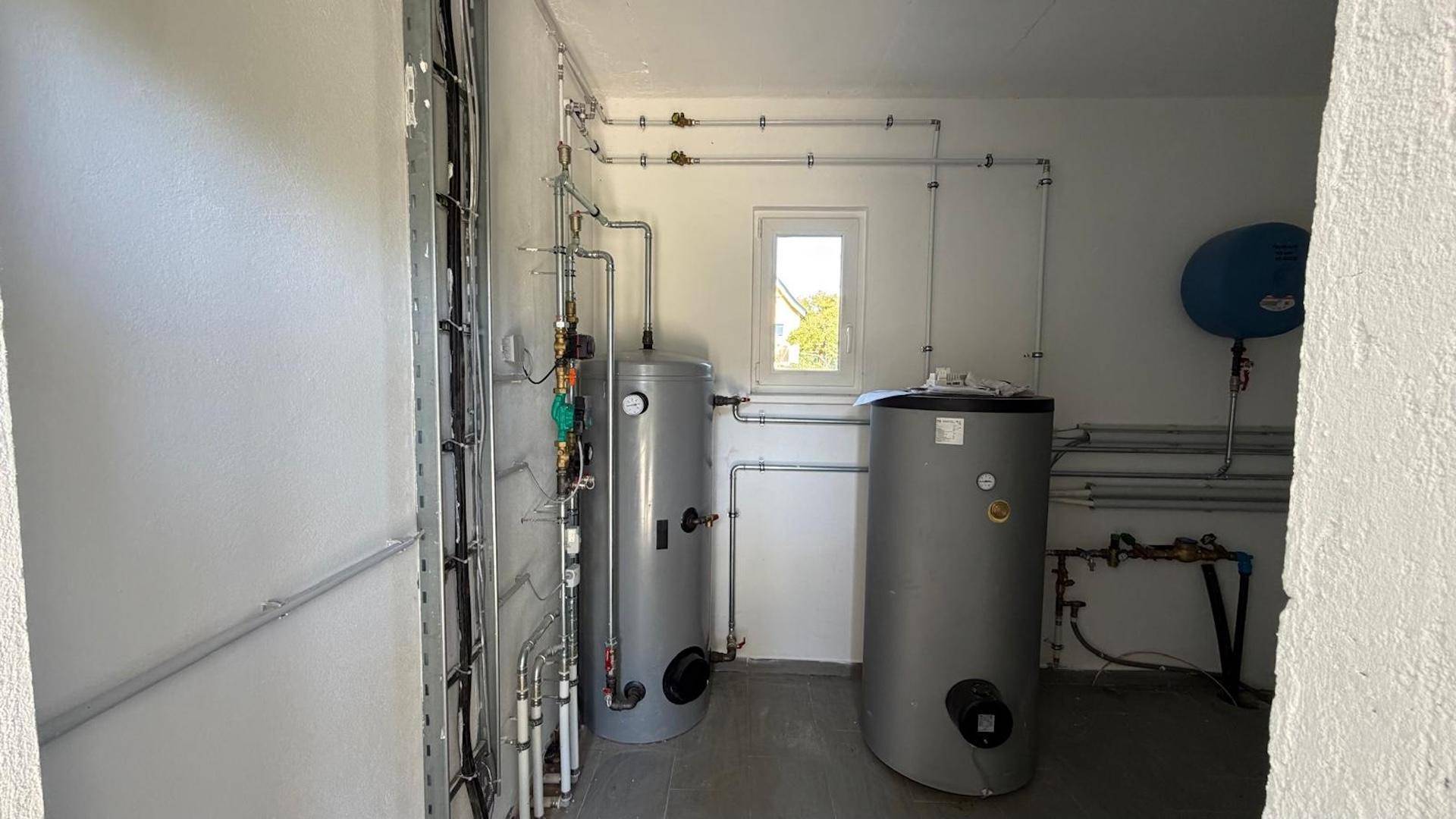 Technikraum mit zwei großen Warmwasserspeichern und umfangreicher Rohrinstallation für die Haustechnik.