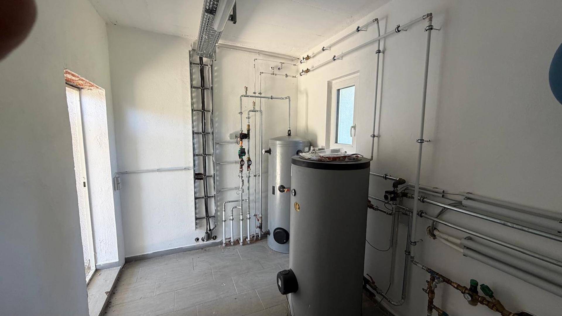 Technikraum mit Heizungs- und Warmwasserspeichern sowie sichtbaren Rohrleitungen.
