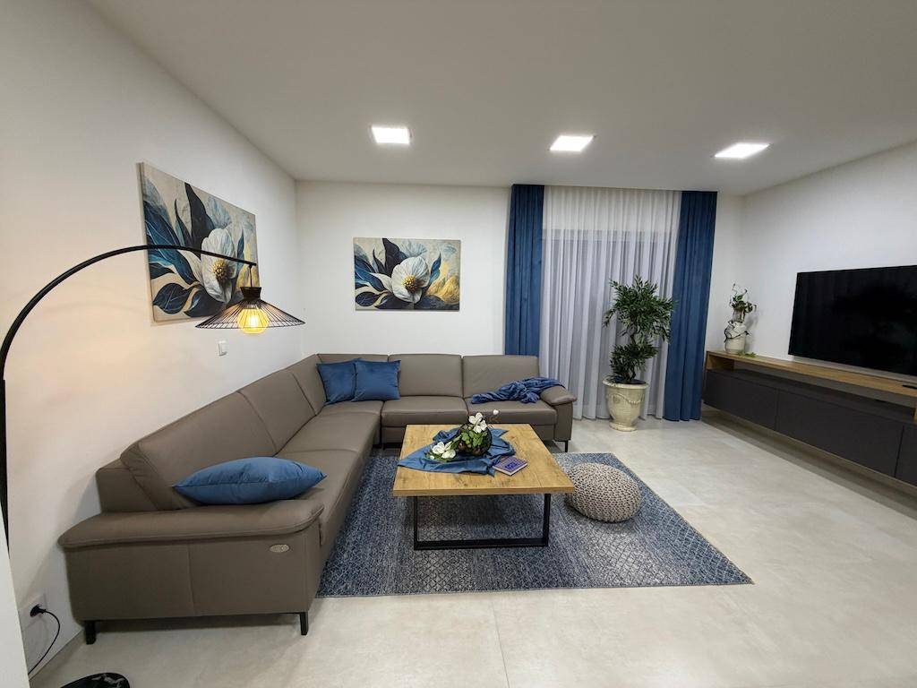 Modernes Wohnzimmer mit beigem Ecksofa, Stehlampe und dekorativen Bildern an der Wand.