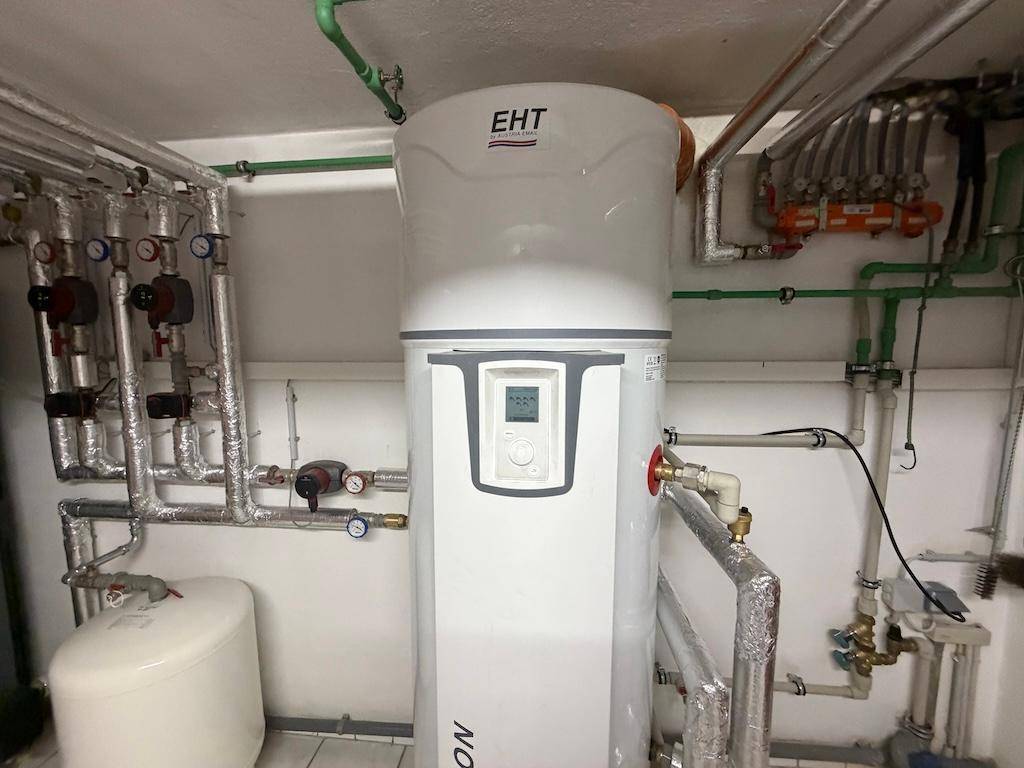 Heizungsraum im Keller mit großem Warmwasserspeicher und zahlreichen Rohrleitungen.