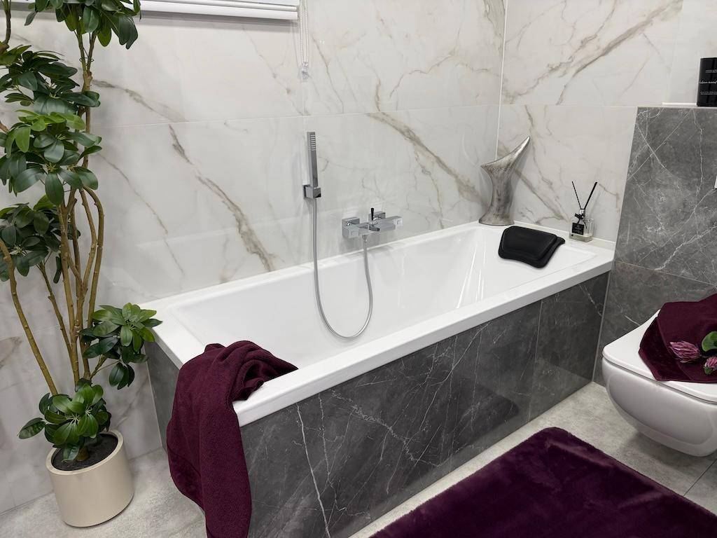 Modernes Badezimmer mit Badewanne, WC und stilvollen Marmorfliesen, ergänzt durch eine Zimmerpflanze.