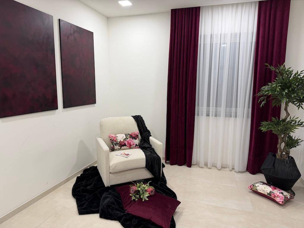 Heller Wohnbereich mit beigem Sessel, dunklen Vorhängen und dekorativen Kunstwerken an der Wand.