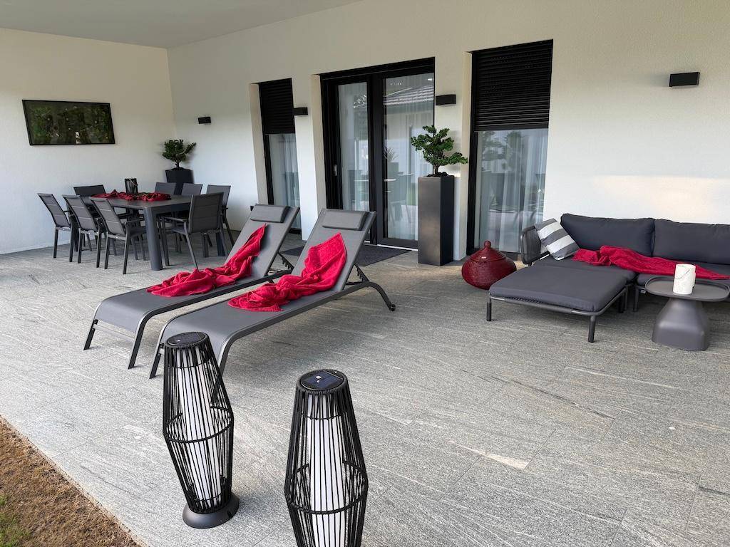 Geräumige überdachte Terrasse mit Liegestühlen und Lounge-Möbeln, ergänzt durch moderne Außenleuchten.