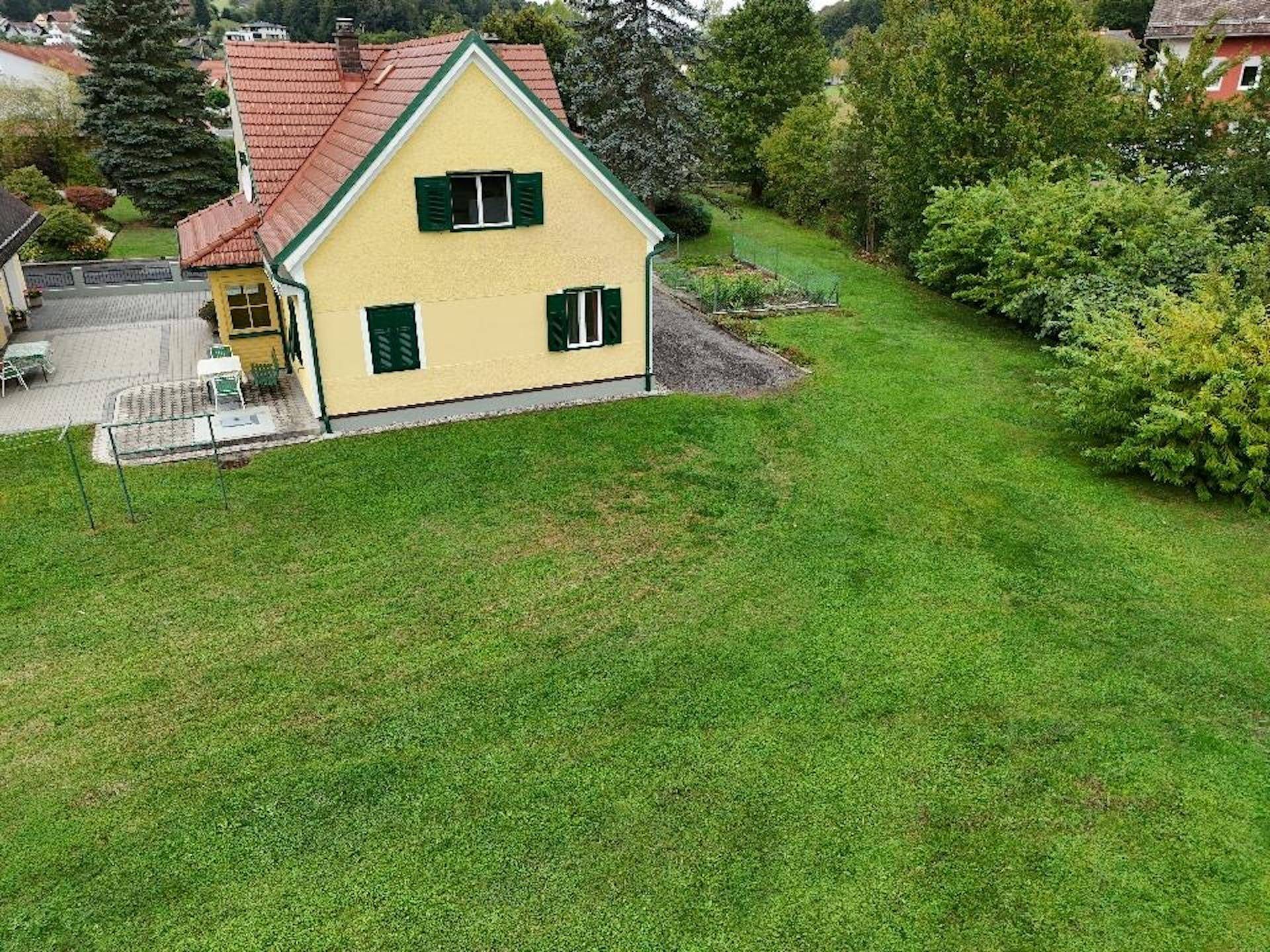 Luftaufnahme des Hauses mit großem Rasenbereich und angrenzendem Garten, umgeben von Natur.