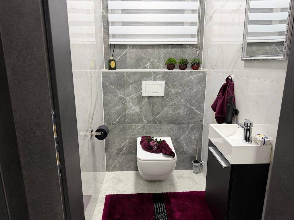 Modernes Gäste-WC mit Wand-WC, kleinem Waschbecken und Fenster mit Jalousie.