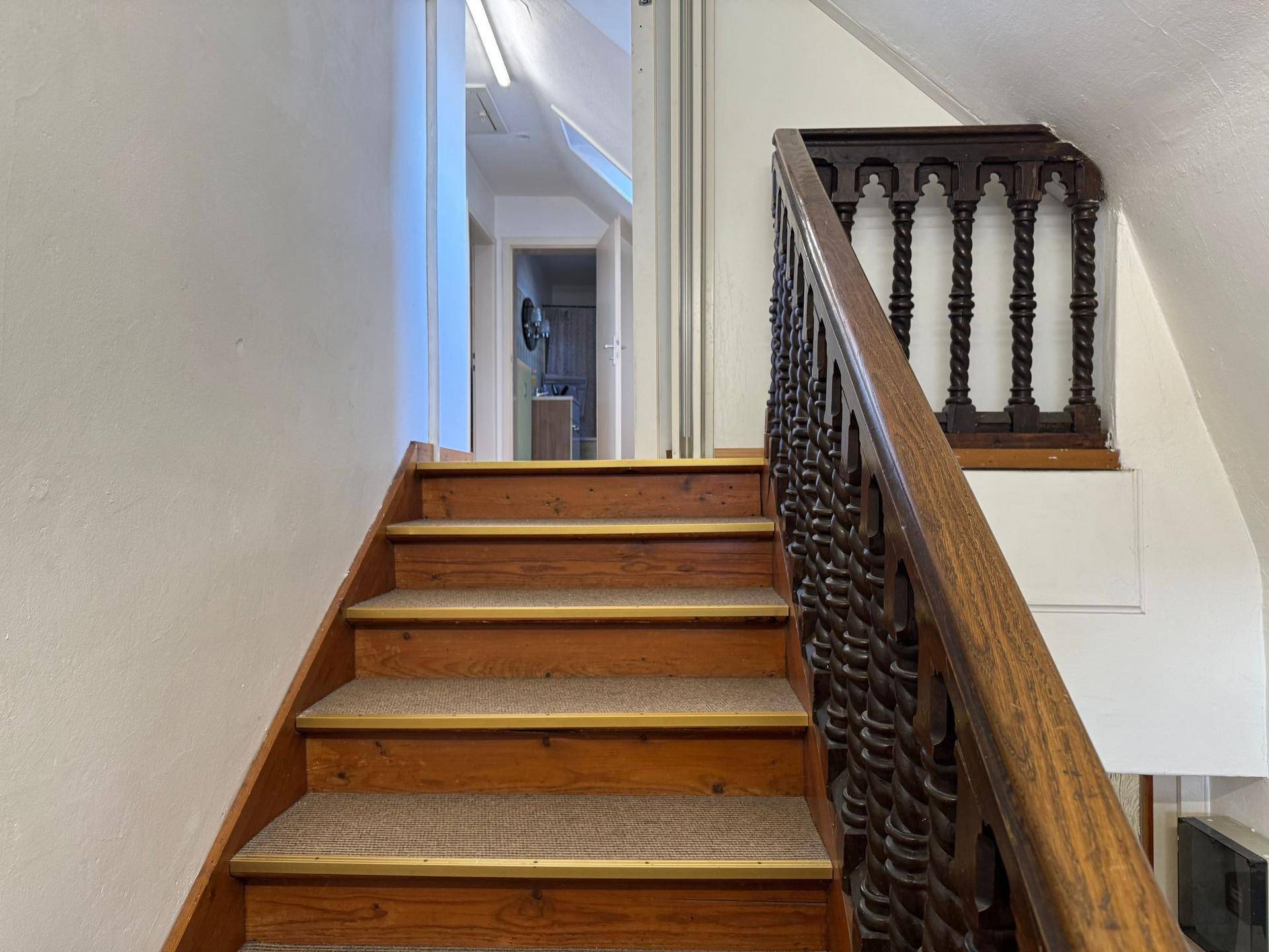 Treppenhaus mit Holztreppe, Teppichläufern und einem verzierten Holzgeländer.