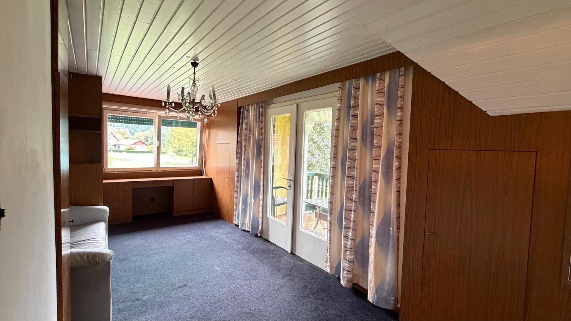 Geräumiges Schlafzimmer mit Teppichboden, Holzdecke und Zugang zu einem Balkon.