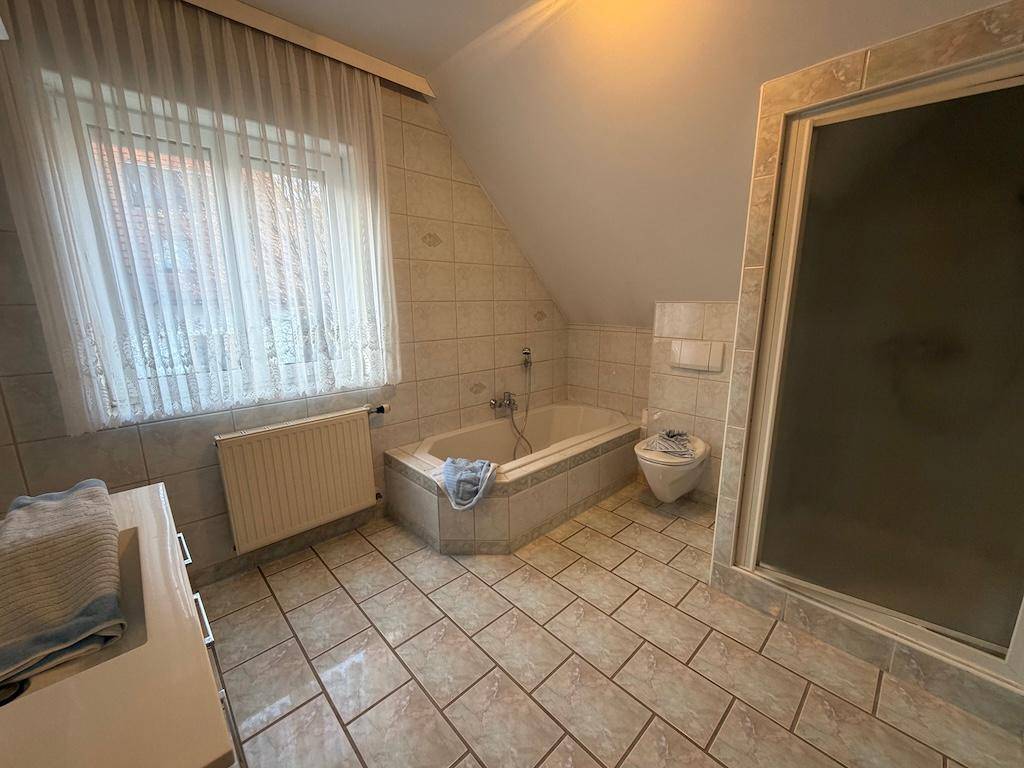 Badezimmer mit Eckbadewanne, Toilette, Duschkabine und Fenster unter einer Dachschräge.