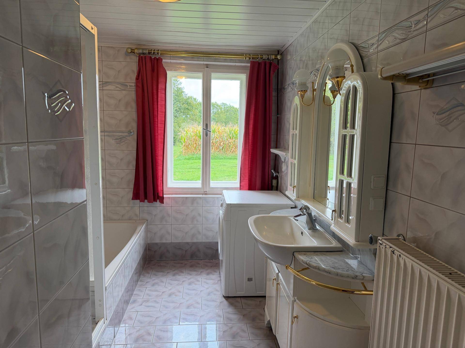Badezimmer mit Badewanne, Waschbecken und Fenster, das einen Blick auf die Natur ermöglicht.
