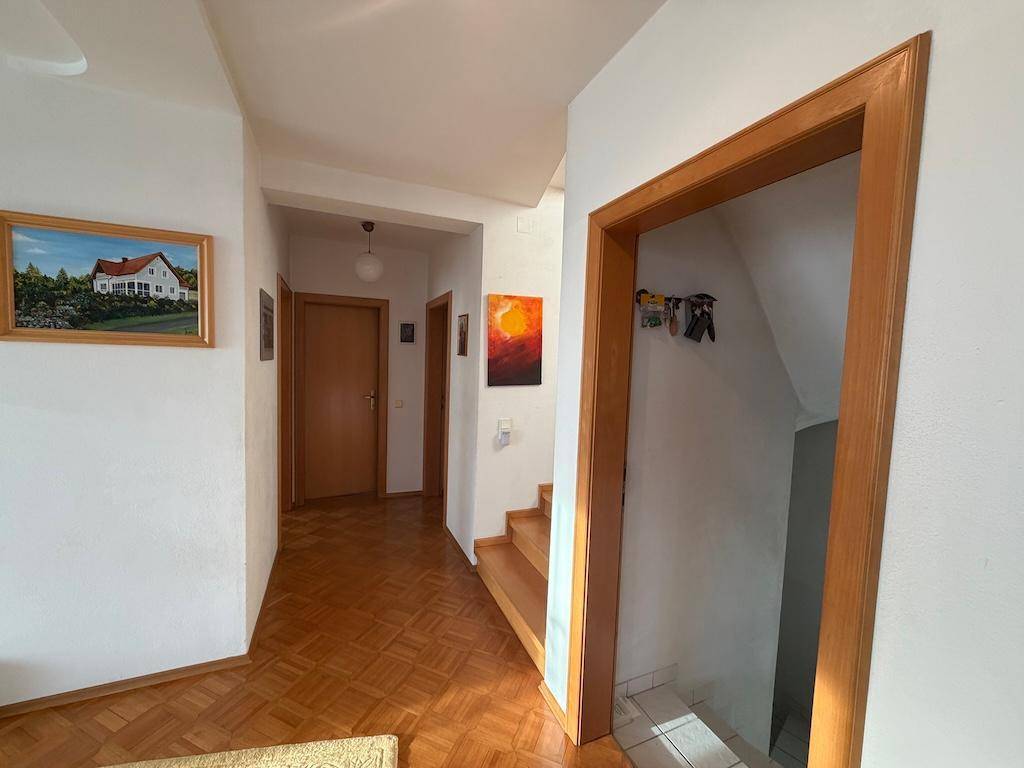 Heller Flur mit Parkettboden, Holztreppe und Zugang zu weiteren Räumen.