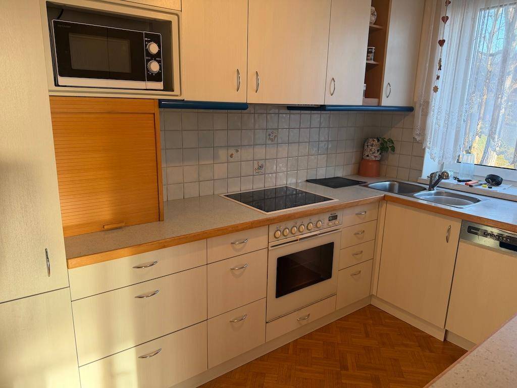 Praktische Küche mit weißen Schränken, integrierten Geräten und Fenster für Tageslicht.