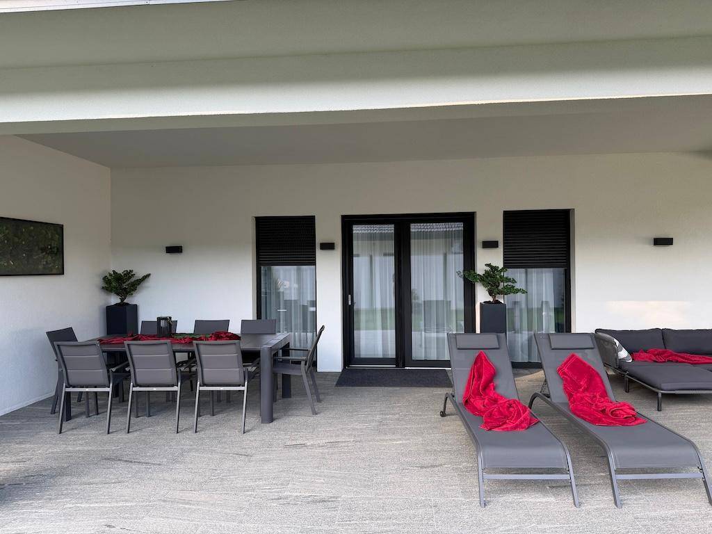 Geräumige überdachte Terrasse mit Esstisch und Liegestühlen, perfekt für Mahlzeiten und Entspannung im Freien.