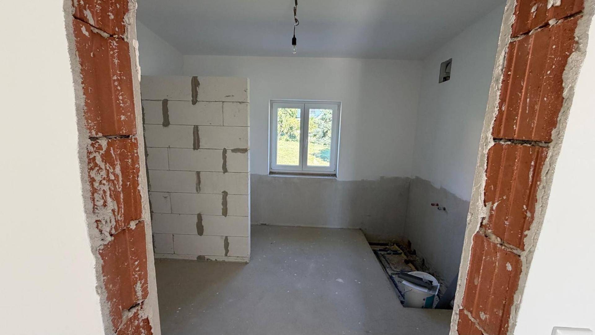 Unfertige Küche mit vorbereiteten Anschlüssen und Fenster, bereit für den Einbau.