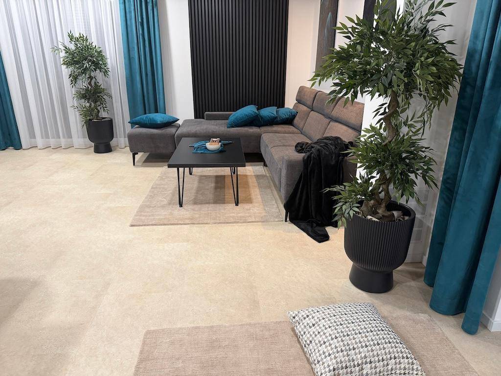 Geräumiges Wohnzimmer mit beigem Fliesenboden, Ecksofa und dekorativen Pflanzen.