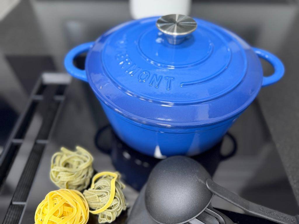 Blauer Kochtopf und frische Pasta auf einer dunklen Arbeitsfläche, bereit für die Zubereitung.