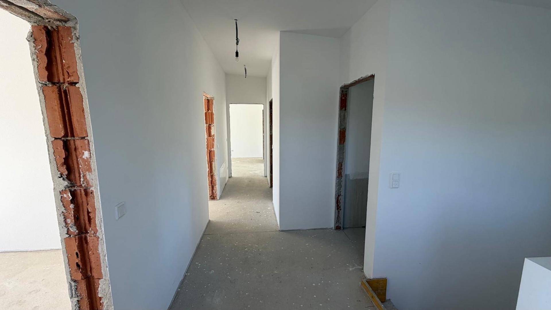 Langer Flur im Rohbau mit offenen Türrahmen und Blick in verschiedene Zimmer des Neubaus.