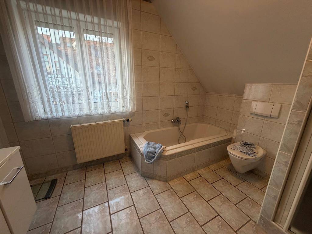 Geräumiges Badezimmer mit Eckbadewanne, WC und Fenster, gefliest in hellen Farbtönen.