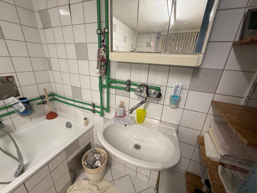 Einfaches Badezimmer im Keller mit Badewanne, Waschbecken und Spiegelschrank.