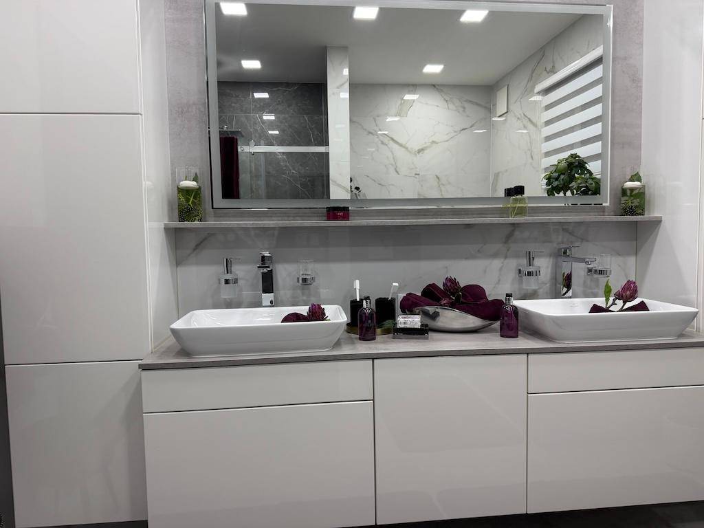 Modernes Badezimmer mit Doppelwaschbecken, großem Spiegel und weißen Unterschränken, hell und geräumig.