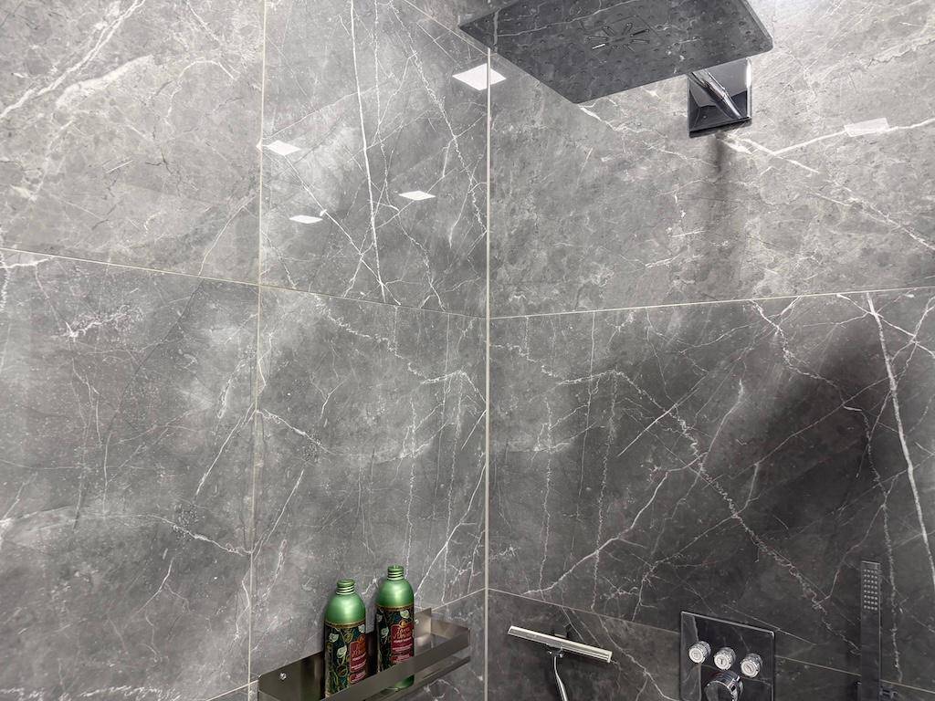 Nahaufnahme einer modernen Regendusche mit eleganten Marmorfliesen im Duschbereich.