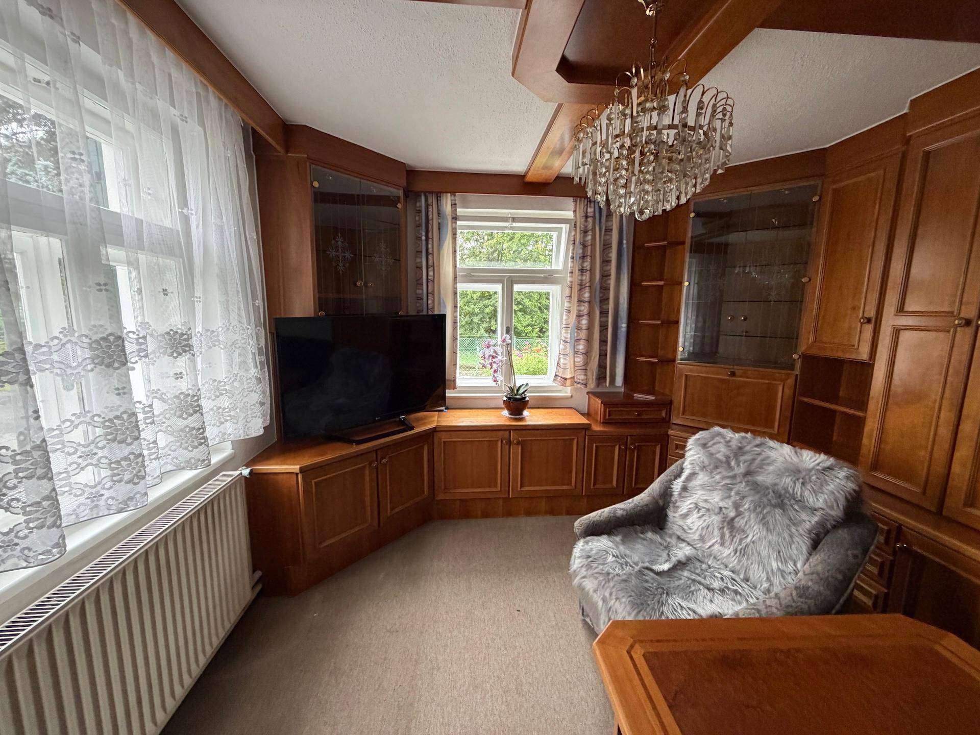 Helles Wohnzimmer mit großen Fenstern, Holzvertäfelung und einem eleganten Kronleuchter.