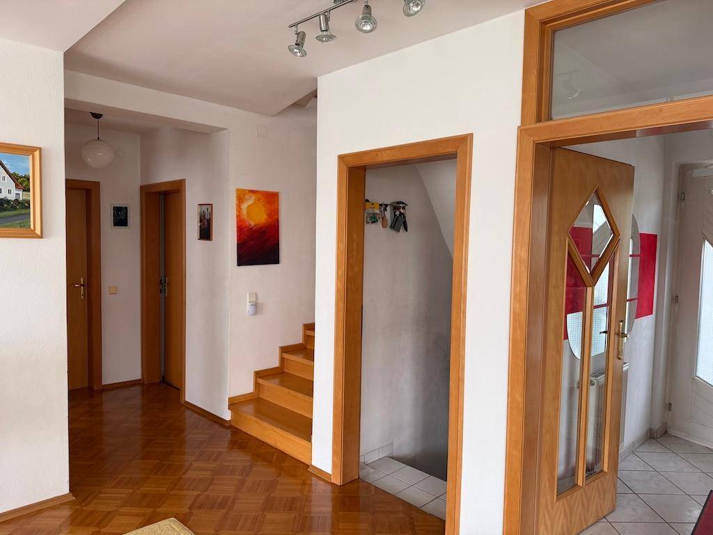 Geräumiger Flur mit Holzparkett, mehreren Türen und einer Treppe ins Untergeschoss.