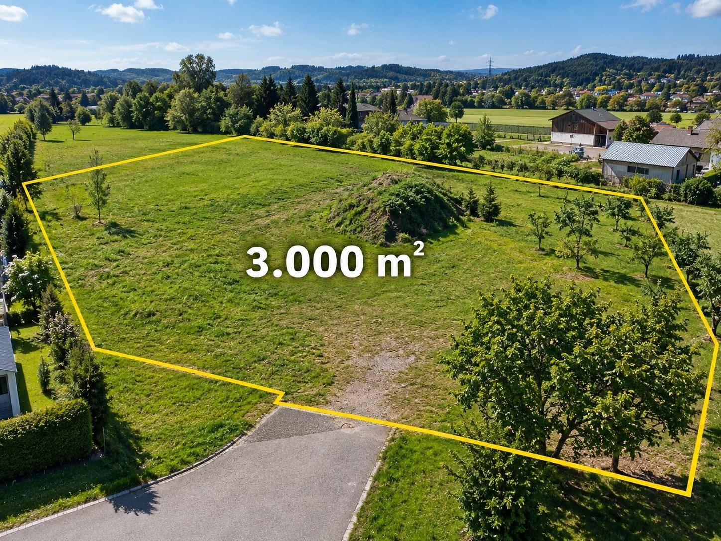 Sonnenbeschienene Luftaufnahme eines großen Baugrundstücks mit grüner Wiese und umliegender Landschaft.