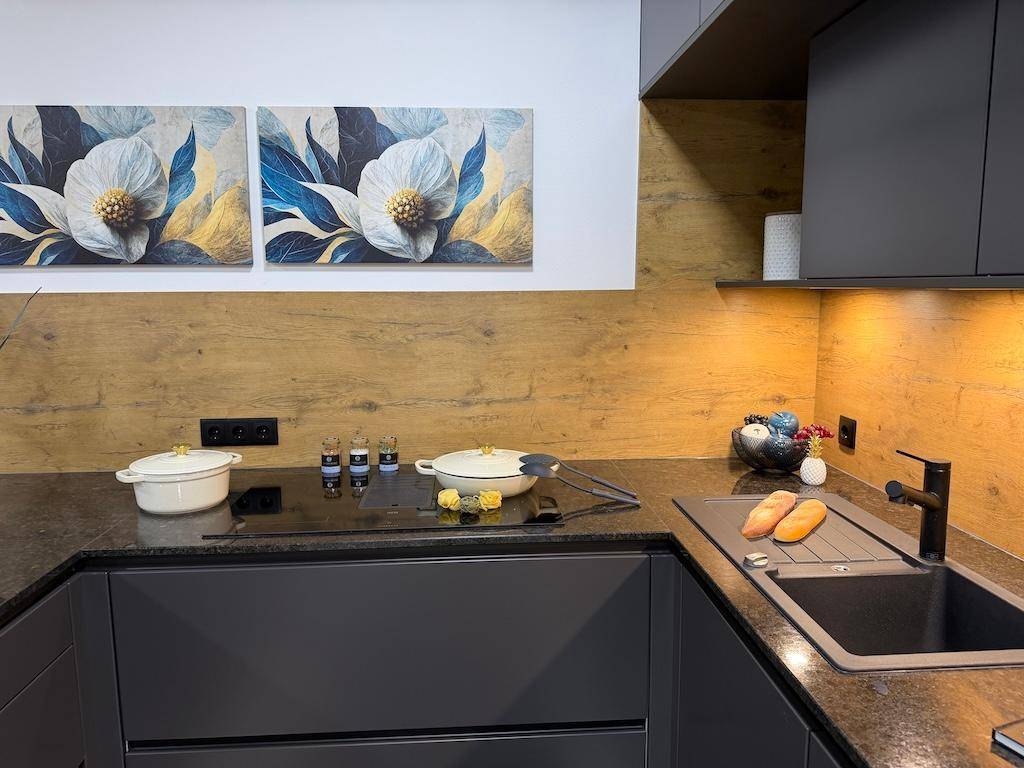 Moderne Küche mit Induktionskochfeld, dunkler Arbeitsplatte und Holzrückwand.