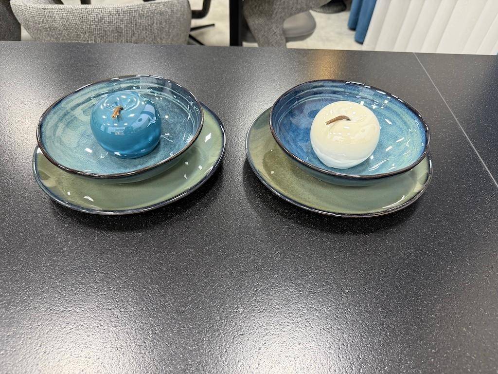 Zwei dekorative Schalen mit kleinen Apfel-Objekten auf einem dunklen Esstisch als Dekoration.