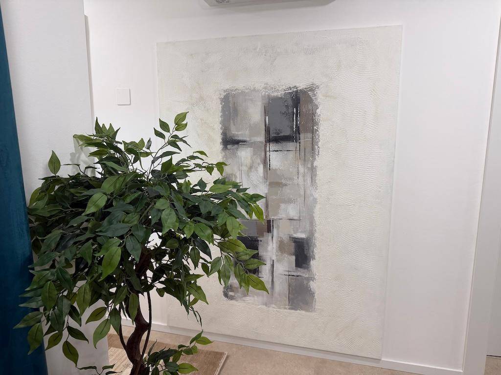 Großes abstraktes Kunstwerk an einer weißen Wand, ergänzt durch eine grüne Topfpflanze.
